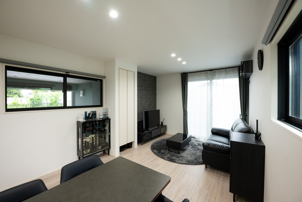 リビングのテレビボードの壁面には素材感を活かしたインテリアタイルを採用。モノトーンの中にも素材感で変化を付けアクセントに。いつでもガレージが見えるようにリビングにも窓を設置。