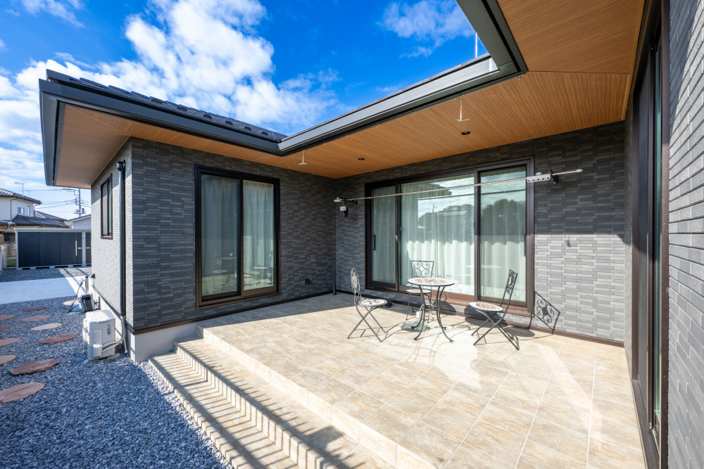 軒を深く取り、夏の日射を抑えつつ雨の日の物干しも可能に。軒天の木目とタイル外壁が落ち着いた雰囲気を作ります。 また、中庭へ続く小道に踏み石を配置するなど、外と内がゆるやかにつなげる工夫が。